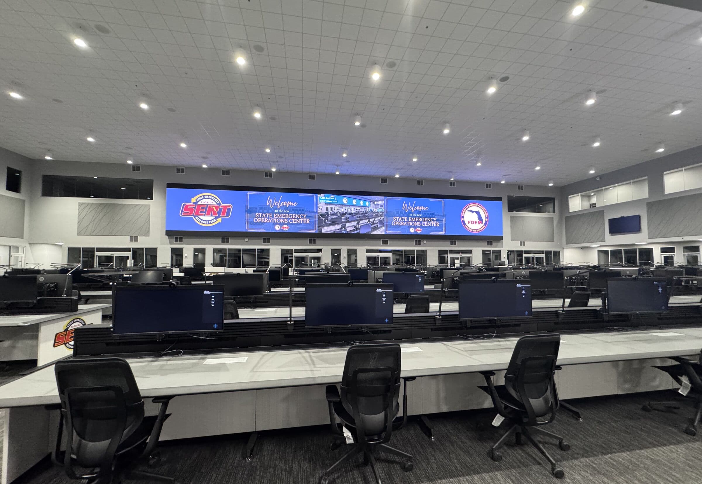 A newly built state emergency operations centre, rows of empty console desks under a full-width video wall reading Welcome to the new State Emergency Operations Center